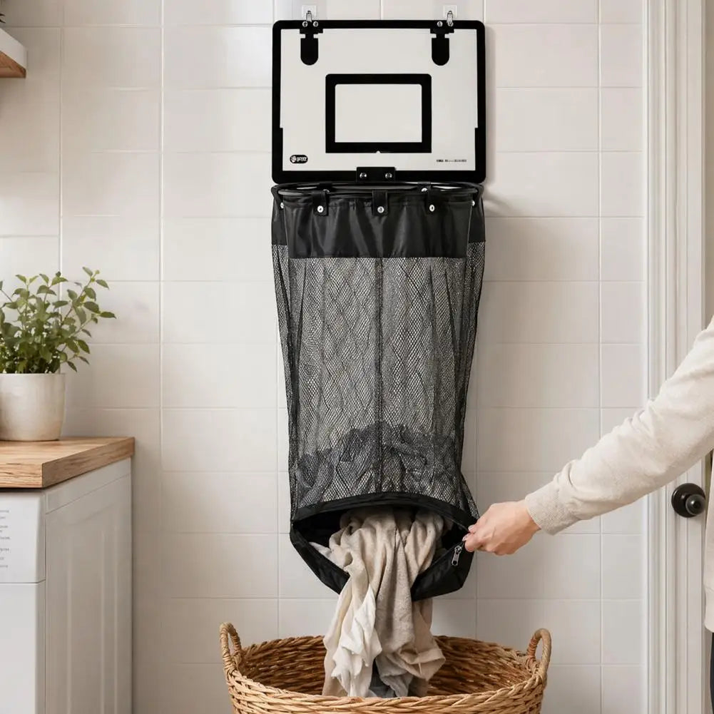 A black and white laundry hamper hanging on a tiled wall, with a person's hand pulling the bottom opening to release a wicker basket of clothes. A plant and washing machine are visible in the background.
Basketball hoop laundry hamper with net attached