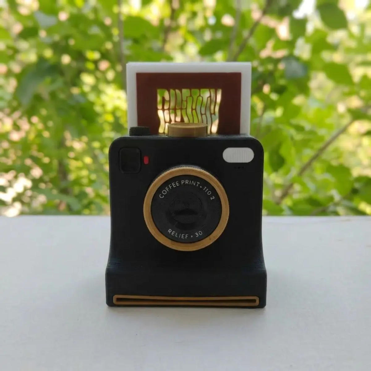 Black camera-shaped latte art stencil tool with a design card inserted