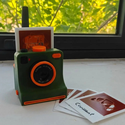 Green camera-shaped latte art stencil tool with interchangeable design cards