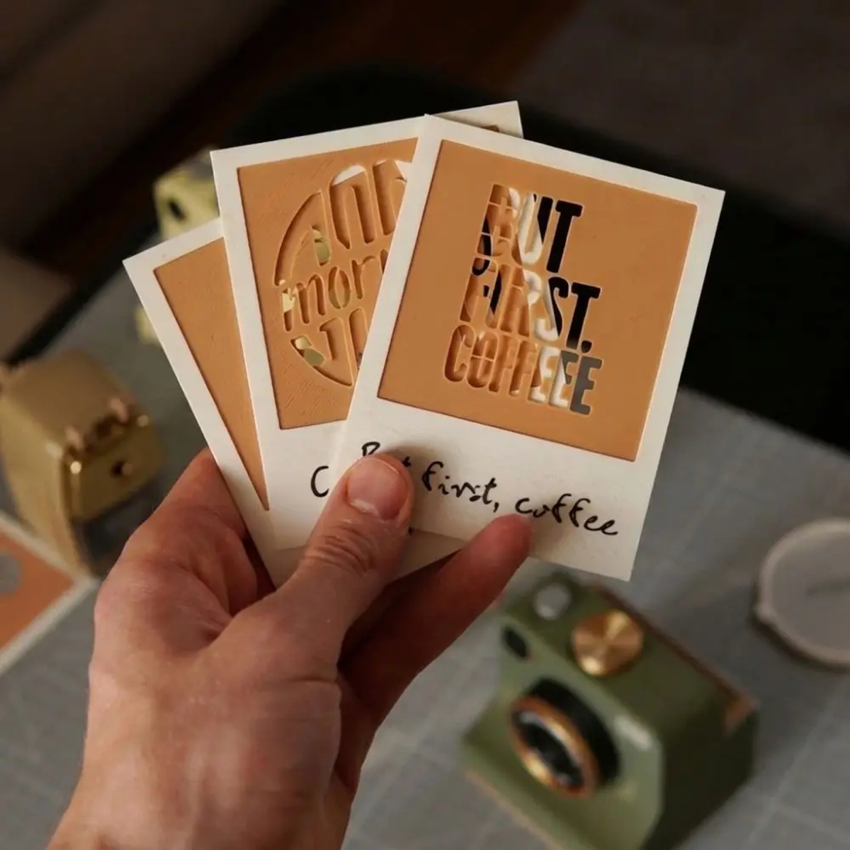 Hand holding interchangeable coffee stencil design cards beside the green tool